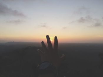 Person hand against sky during sunset