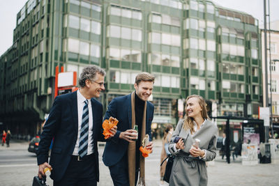 Smiling business professionals talking while holding food and drink in city