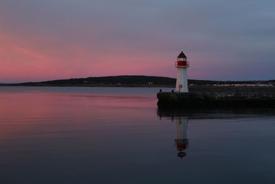 Lighthouse by building against sky during sunset