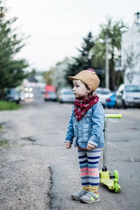 Cute girl standing by push scooter on road