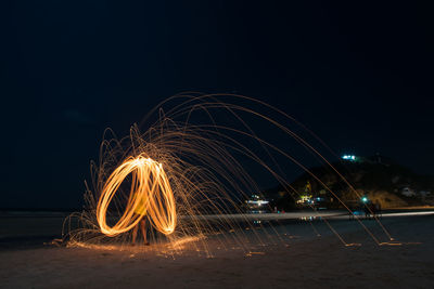 Illuminated light trails on beach against sky at night