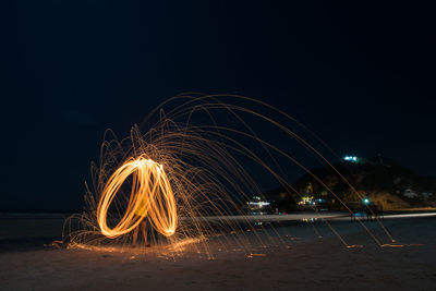 Person spinning wire wool on beach against sky at night