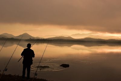Silhouette man fishing in lake against sky during sunset