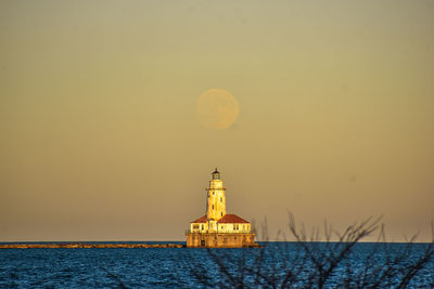 Lighthouse with moonrise against sky during sunset