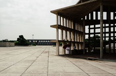 Rear view of man standing on footpath by building against sky