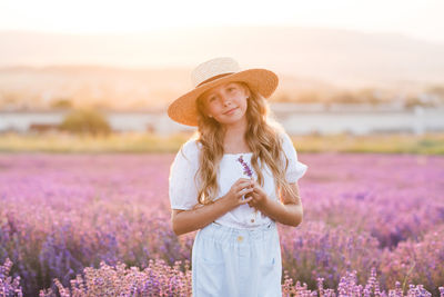 Cute child girl 8-9 year old with long curly blonde hair wear straw hat in bloom lavender field