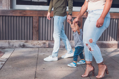 Family of three playing in downtown, parents holding baby boy's hands