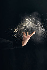 Close-up of hand throwing talcum powder against black background