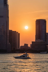 Modern buildings by sea against sky during sunset