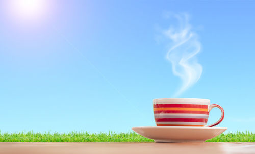 Close-up of coffee cup on field against blue sky