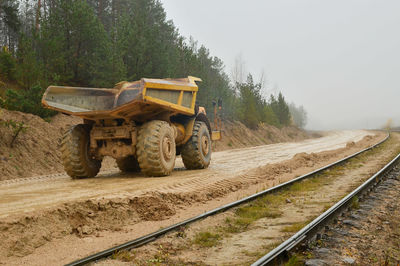 Railroad tracks by road amidst trees against sky