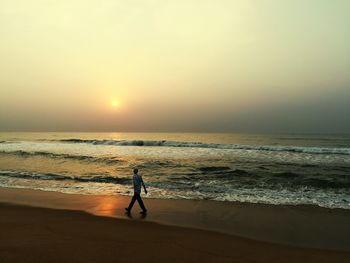 Silhouette man walking on beach against sky during sunset