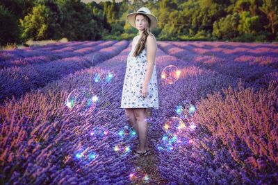 Portrait of woman standing by purple flowers on field