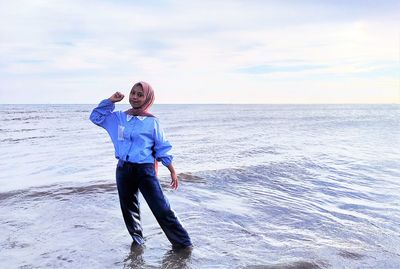 Full length of young woman standing on beach against sky