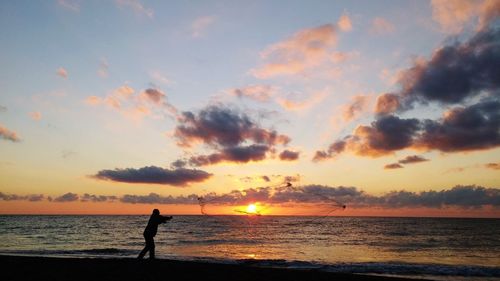 Silhouette person standing on beach against sky during sunset