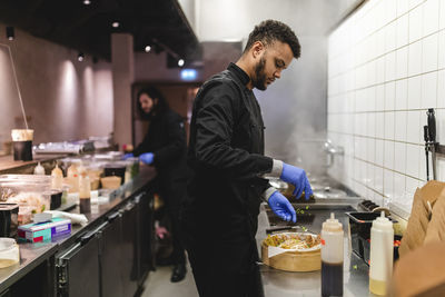 Male waiter sprinkling scallion on dumplings in bowl over kitchen counter at restaurant