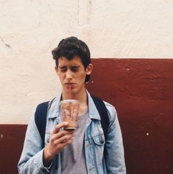 Young man with eyes closed having drink against wall