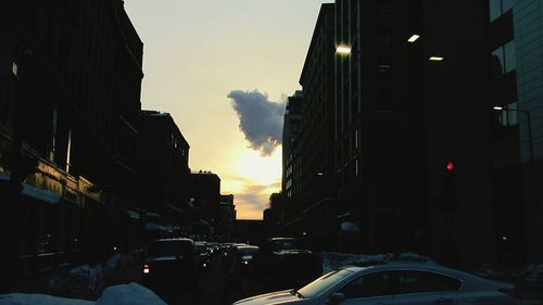 Cars on street in city against sky during sunset