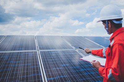 Engineer checking solar panel against cloudy sky