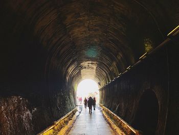 Rear view of people walking in illuminated tunnel