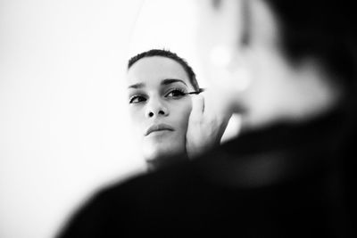 Reflection of young woman applying mascara on mirror