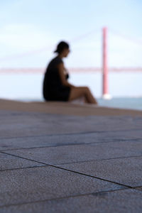 Side view of woman sitting on beach against sky