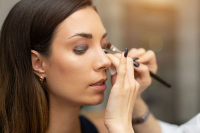 Cropped image of beautician applying make-up to fashion model in studio