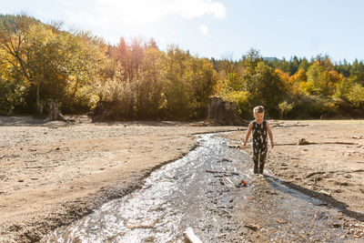 Young, smiling boy splashes in creek in the autumn sunshine