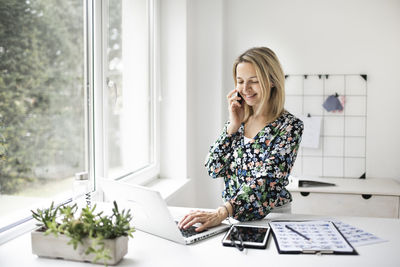 Businesswoman talking on phone while using laptop