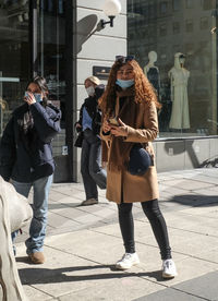 Full length of woman photographing on footpath in city