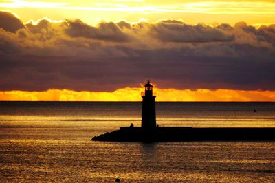 Lighthouse by sea against sky during sunset