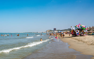 People at beach against clear blue sky