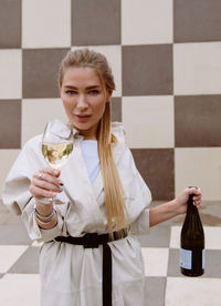 Young woman tasting white wine against chessboard background