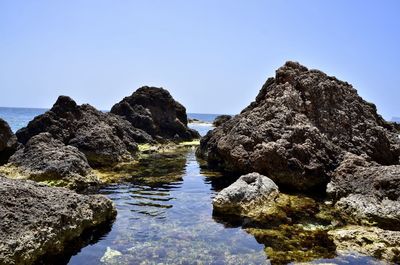 Rocks on sea shore against clear blue sky