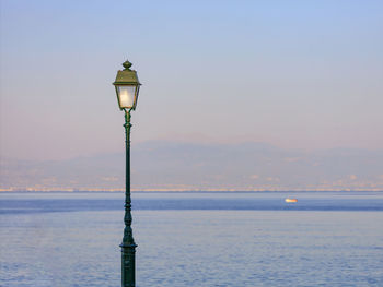 Street light by sea against sky during sunset