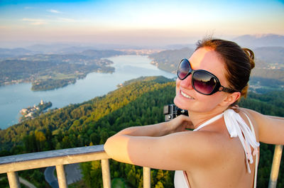 Portrait of woman wearing sunglasses standing by railing against mountain