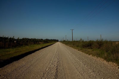 Road amidst field against clear blue sky