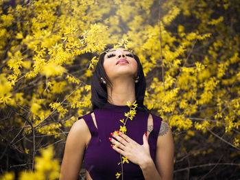 Young woman standing holding yellow flowers against plants
