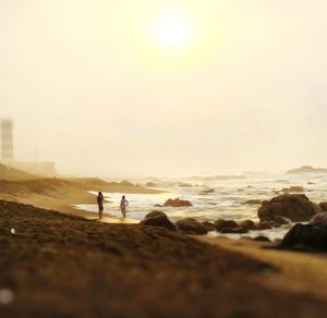 People standing on beach against sky during sunset