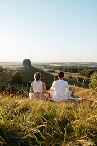 Man and woman practicing yoga and meditation outdoors at sunset with nature miracle giant stone