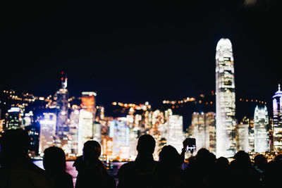People on illuminated buildings against sky at night