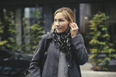 Mid adult businesswoman wearing earphones while crossing street