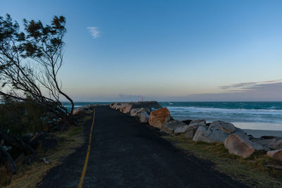 Road by sea against sky during sunset