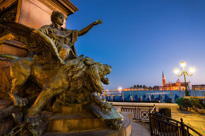 Statue against illuminated buildings in city against clear sky