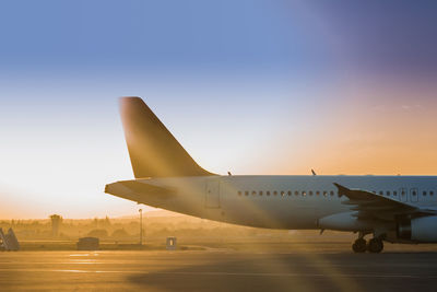 Airplane on airport runway against sky during sunset