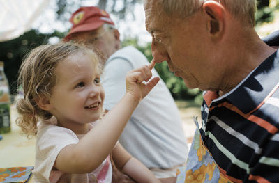 Cute granddaughter touching grandfather's nose while sitting in yard