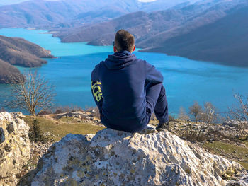 Rear view of man sitting on rock against valley