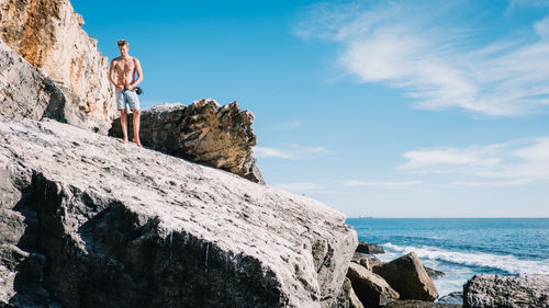 Low angle view of man standing on cliff by sea against sky