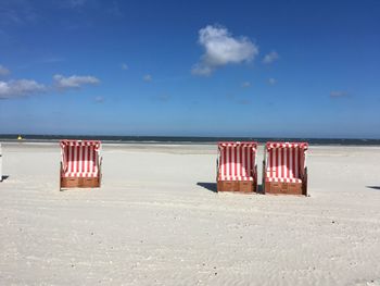 Hooded chairs on beach against sky