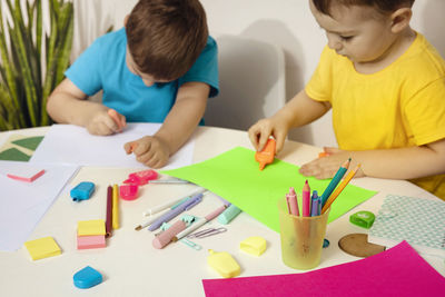 Happy kids with yellow and blue shirts doing arts and crafts together at their desk. 